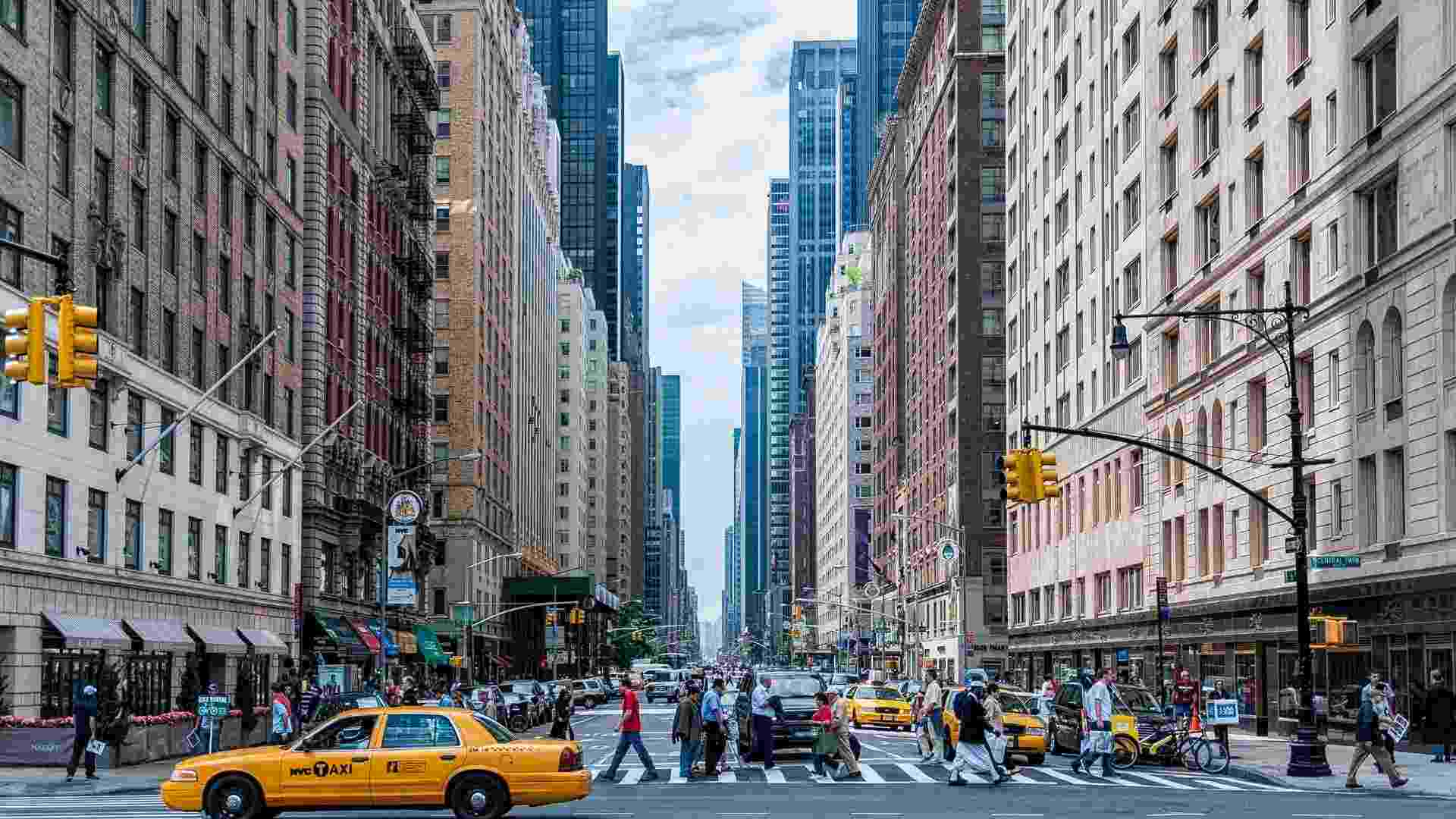 Busy city street in New York City with yellow taxis, pedestrians, and tall buildings.