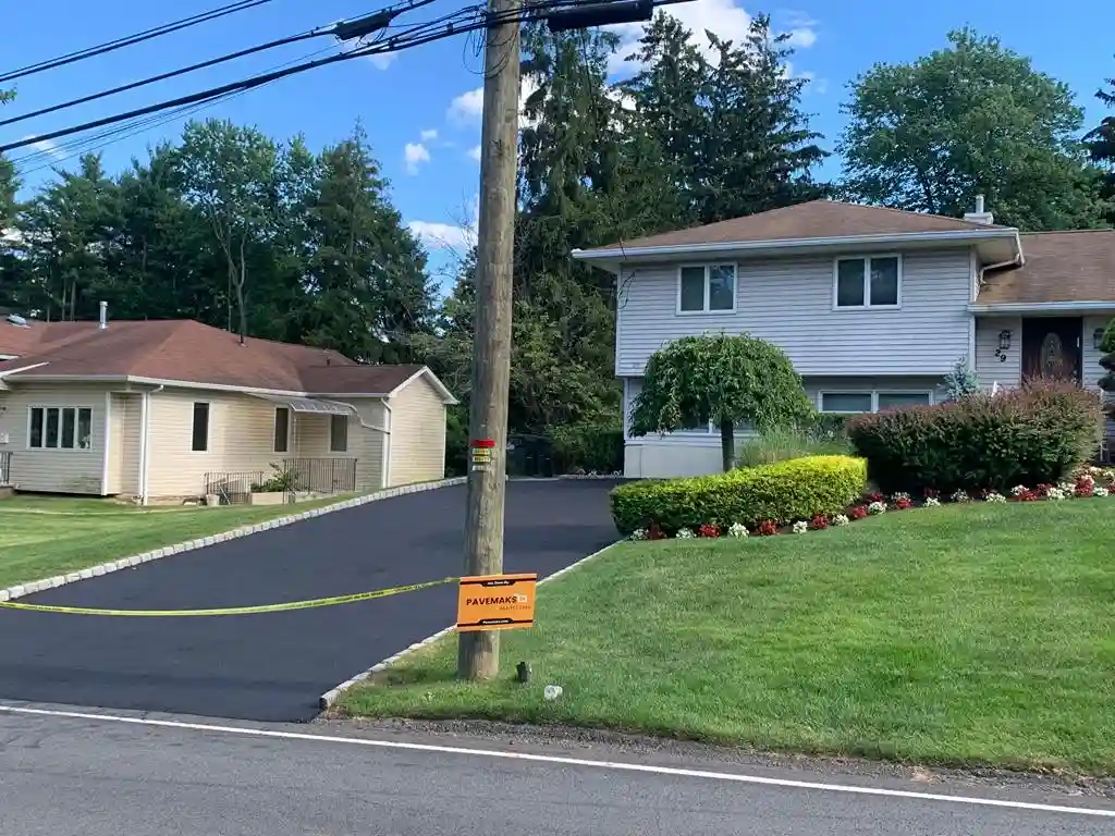 Freshly paved black asphalt driveway at a residential home, with caution tape marking the area.