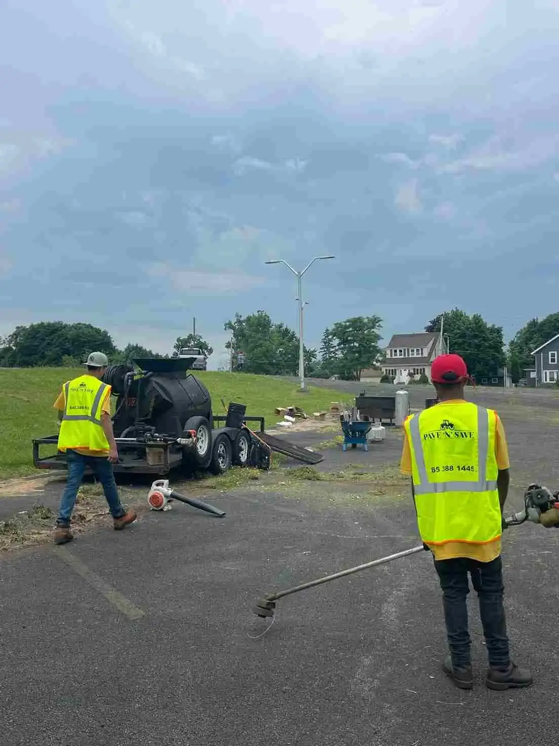 Construction workers with "Pave N Save" vests walking and cleaning the area using leaf blowers.
