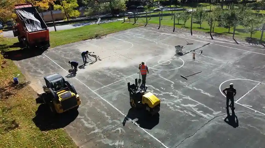 Workers cleaning and maintaining a basketball court, using various machinery and tools