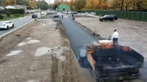 A large paving machine is in operation, and a truck is unloading materials